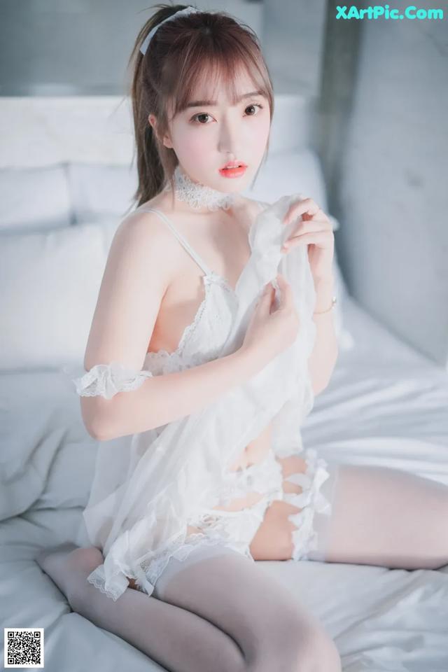 A woman in a white lingerie sitting on a bed.