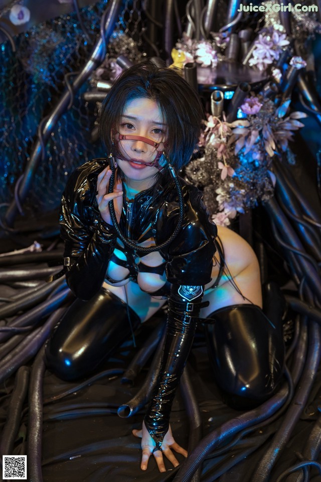 A woman in a black latex outfit sitting on a bed of wires.