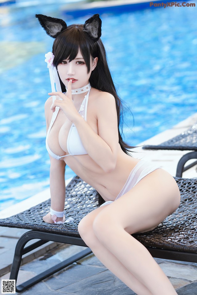 A woman in a white bikini sitting on a lounge chair by a pool.