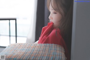 A woman in a red shirt and white panties sitting on a bed.