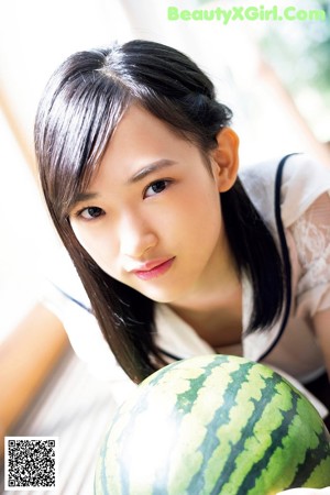 A woman holding a watermelon in front of her face.