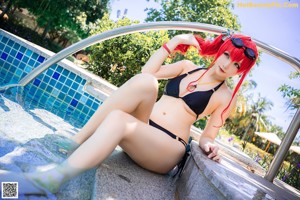 A woman in a black bikini sitting on a ladder by a pool.