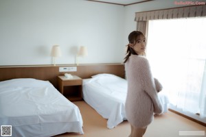 A woman in a pink sweater and white panties on a bed.