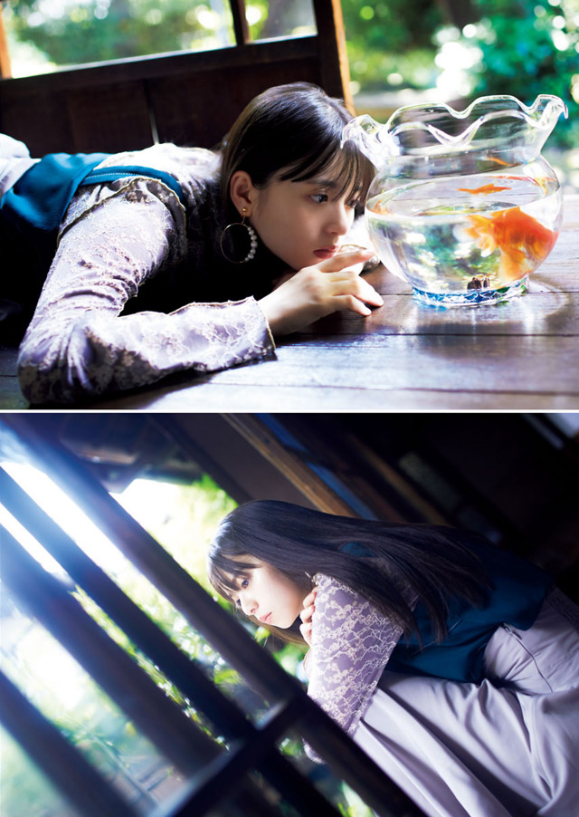 A woman laying on a window sill next to a fish bowl.