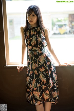 A woman with long black hair standing in front of a window.