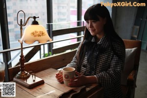 A woman sitting at a table holding a cup of coffee.