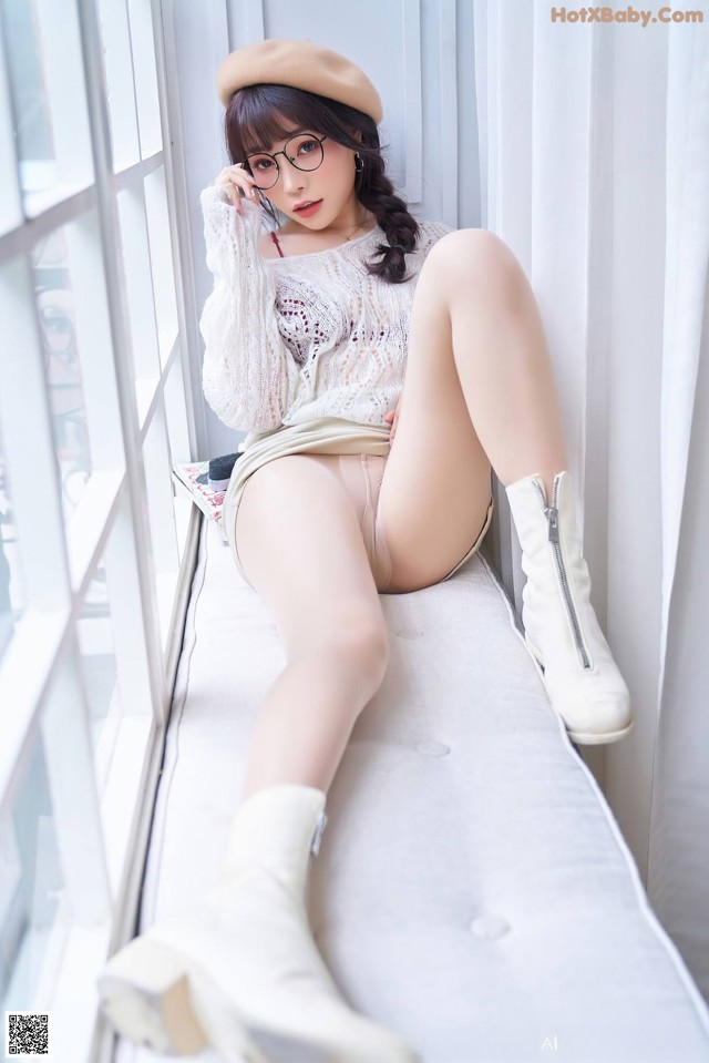 A woman sitting on a window sill wearing white boots and a beret.