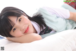 A woman in a school uniform sitting on a bed.