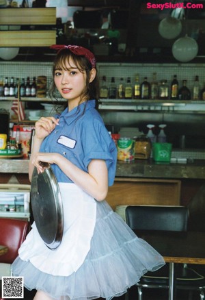 A woman in a blue shirt and white apron standing in front of a mirror.