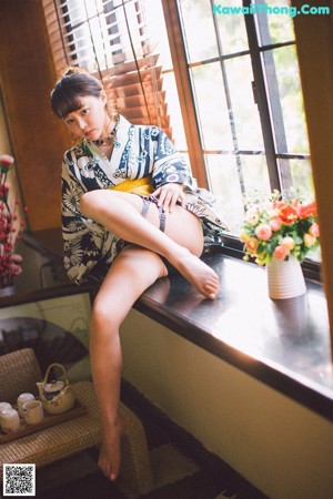 A woman sitting on a window sill next to a vase of flowers.