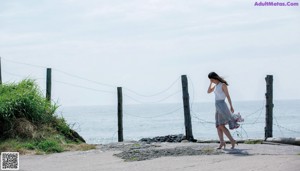 A naked woman standing on a rocky beach next to the ocean.